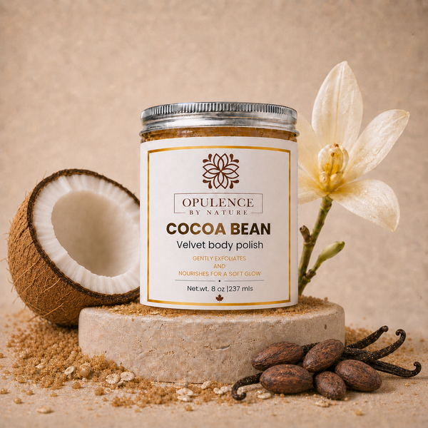 A jar of Opulence by Nature Cocoa Bean Velvet Body Polish is displayed on a stone pedestal with a coconut half, vanilla beans, and a white orchid flower against a textured beige background.